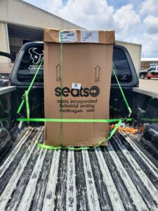 Small package on top of a large boxed cargo strapped upright to the back of a pickup truck