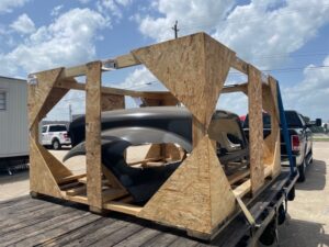 Exterior car frame packaged inside a wooden box strapped to a flat bed connected to a pickup truck