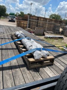 Two plastic-covered rods strapped down over a wooden crate flooring on a flat bed