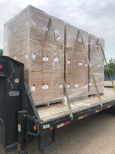 Three plastic-wrapped stacks of boxed packages strapped upright to a truck flat bed